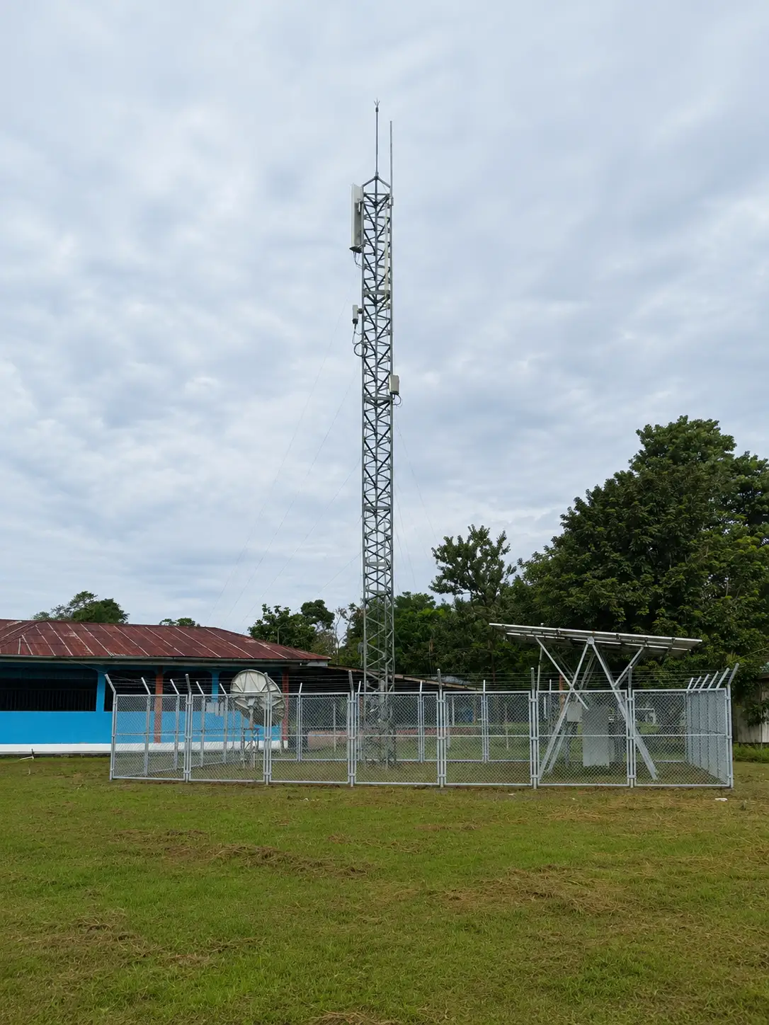Torre de telecomunicaciones en una explanada, con caseta de equipos y cerco perimétrico.