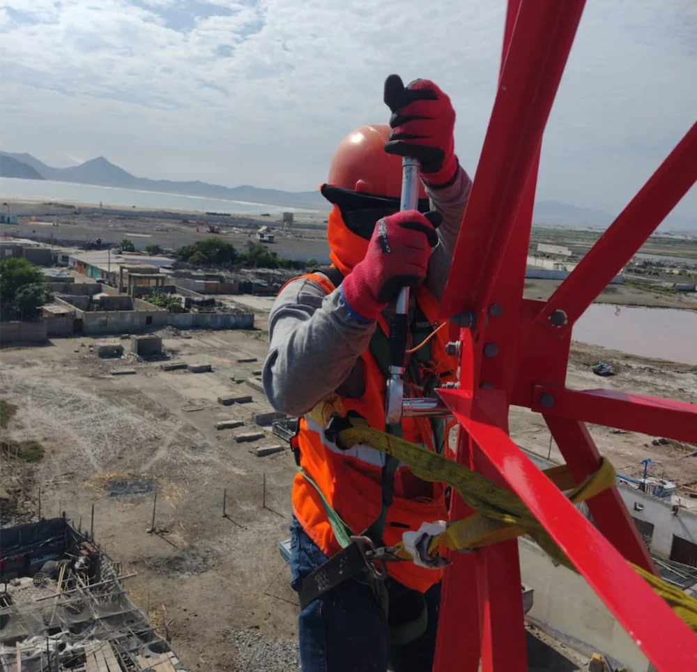 Trabajador con arnés y casco ajustando la pernería de una estructura metálica de torre durante el montaje.