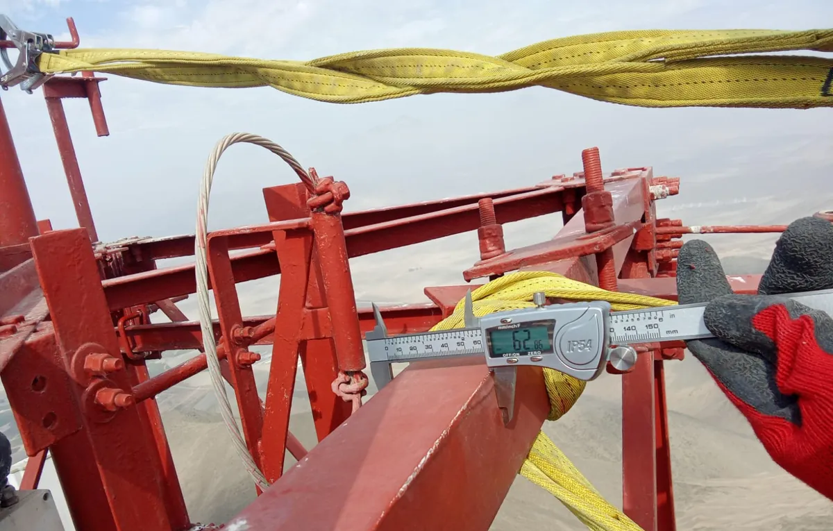Técnico midiendo con un calibrador digital un perfil de la torre, asegurado con eslingas amarillas.