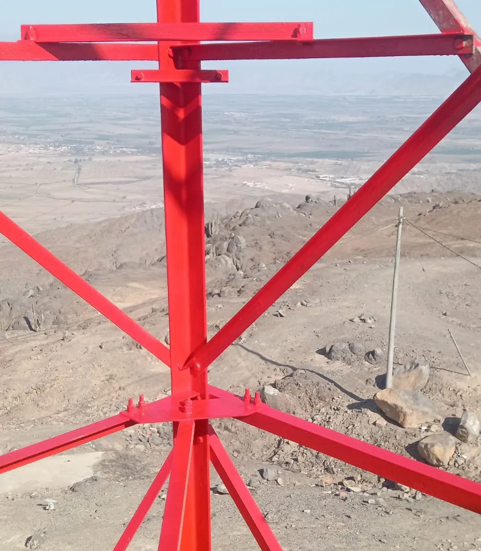 Torre recién pintada de rojo vista desde lo alto, con terreno árido al fondo.