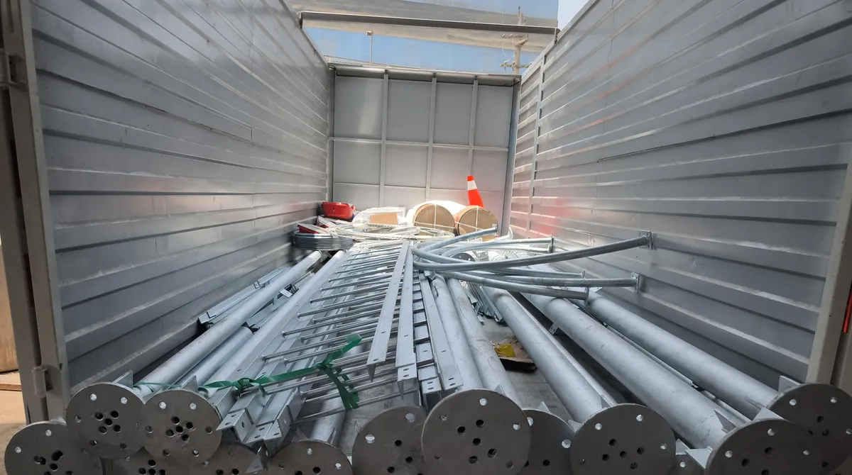 Camión cargado con postes y tubos galvanizados con sus bridas de base, escaleras de torre y rollos de cable, listo para el despacho.