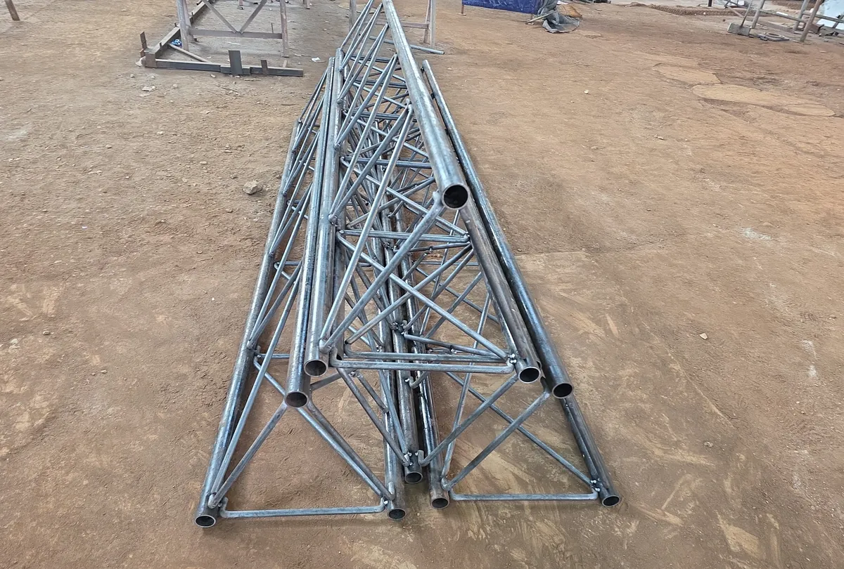 Tramos de torre de celosía tubular apilados en el piso de un taller, listos para el despacho.
